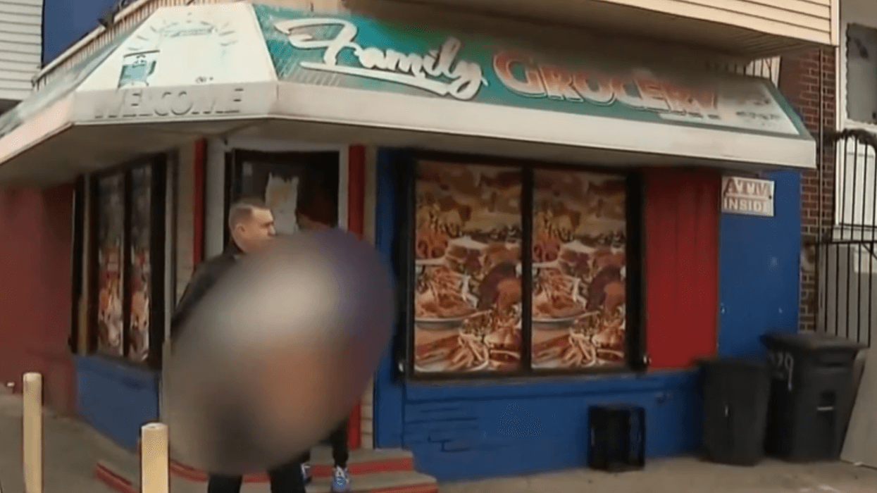 Police officer carries 11-month-old baby (blurred) out of a corner store in Juniata Park
