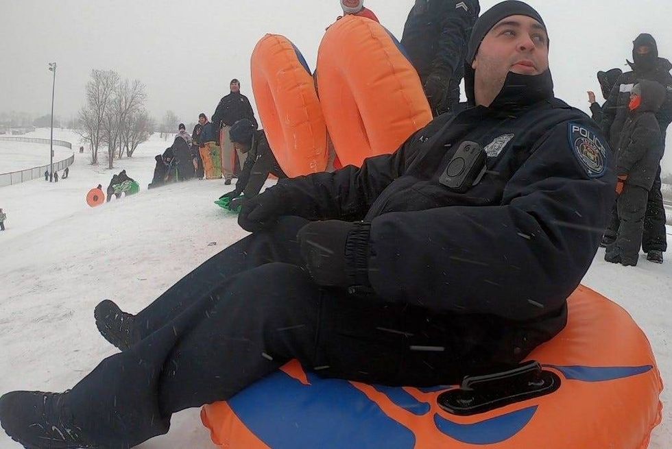 Police officer sitting on orange sledding tube on top of snowy hill