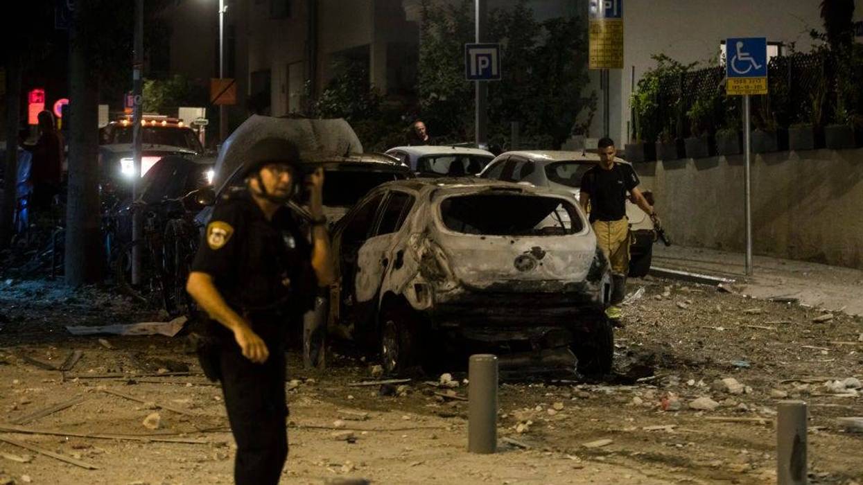 Police officer stand near a burned car at a scene where a rocket fired from Gaza strip hit a building on October 7, 2023 in Tel Aviv, Israel.