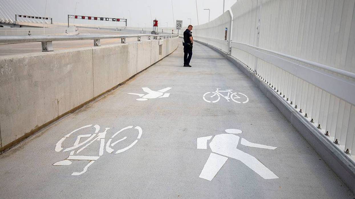 Police officer stands on the Gordie Howe International Bridge path. There are white biking and walking symbols in front of him.