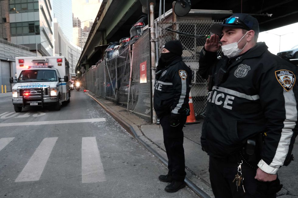 Police officers pause as the body of NYPD officer Wilbert Mora is transferred in an ambulance from NYU Langone Hospital to the medical examiner
