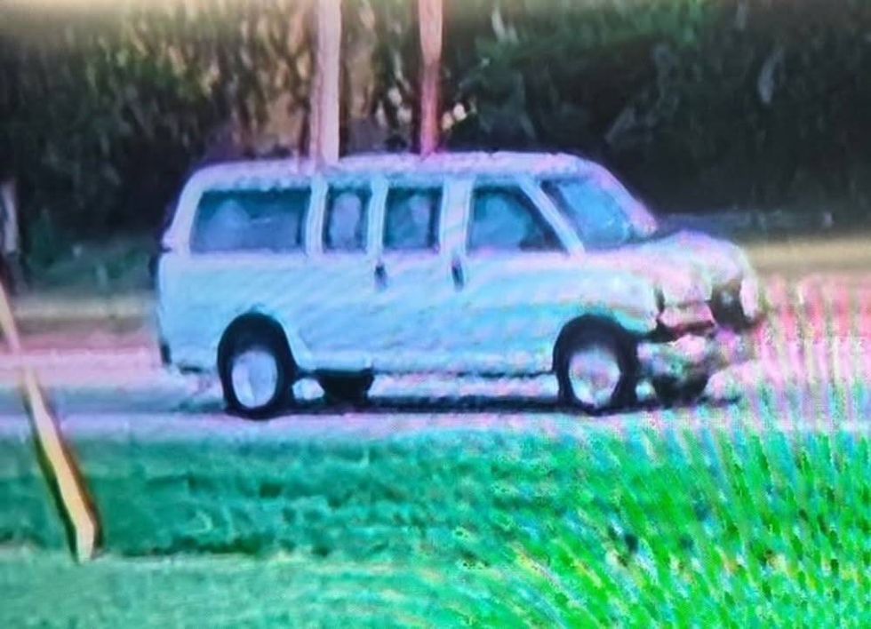 Poor quality image of a white passenger van with a crumpled front end, parked by a roadside.