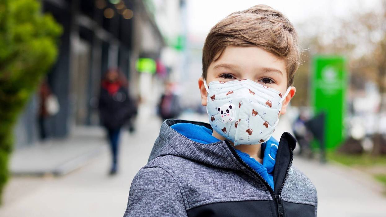 Portrait of smiling boy wearing protective face mask while walking in the city during COVID-19 pandemic.