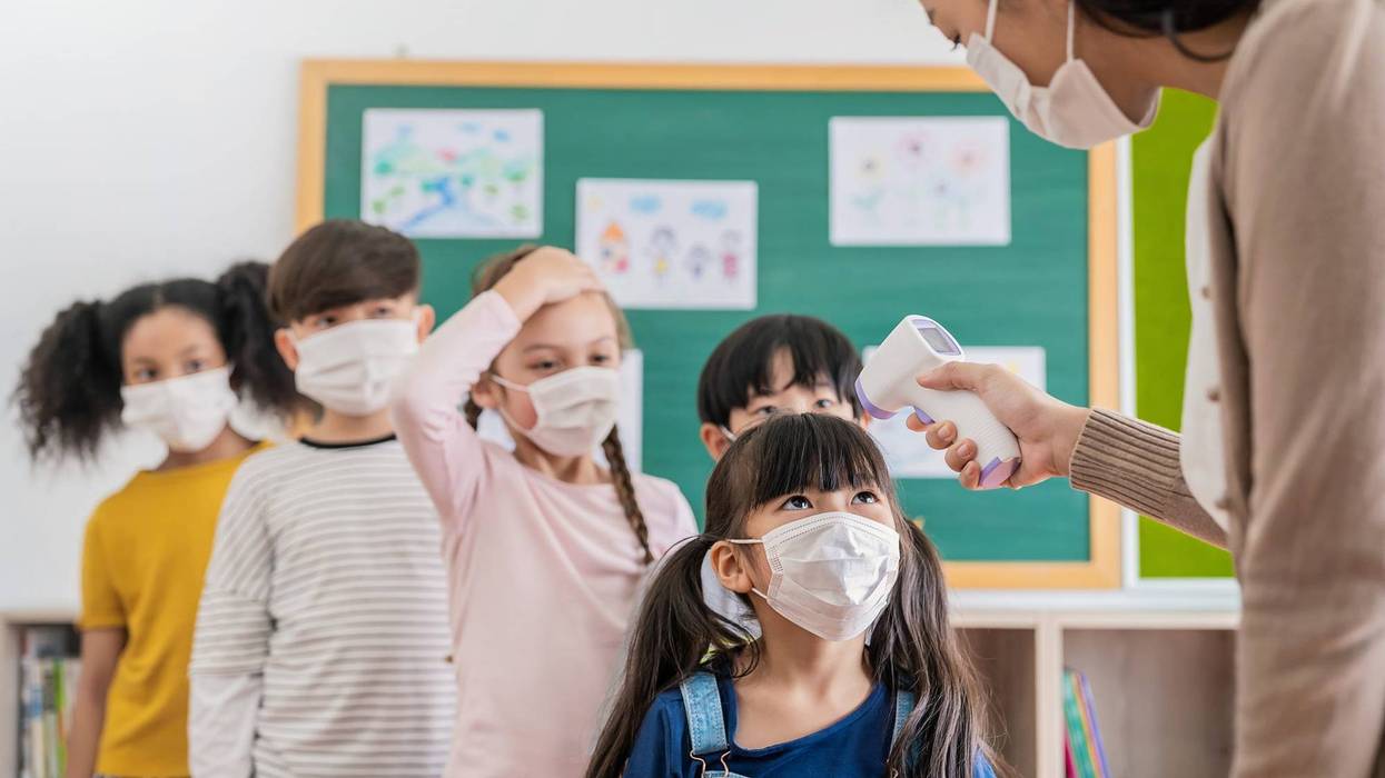 Portrait of students in medical mask in classroom, covid-19 outbreak. Teacher and kids with thermometer at preschool entrance. Social distancing, coronavirus prevention. Temperature check in at school. - stock photo