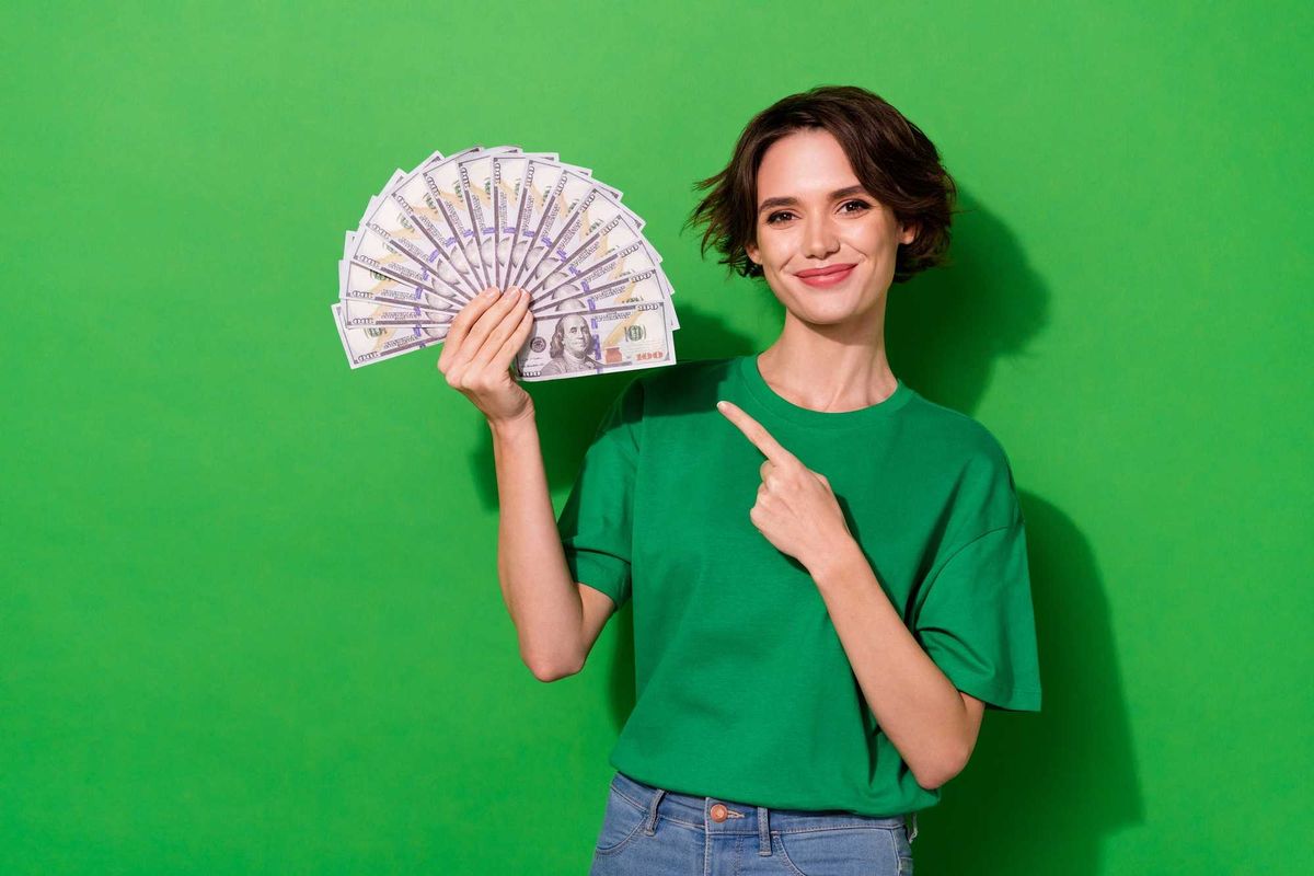 Portrait of successful pretty lady direct finger dollars banknotes isolated on green color background.