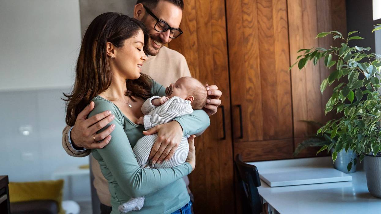 Portrait of young happy man and woman holding newborn cute babe dressed in white unisex clothing.