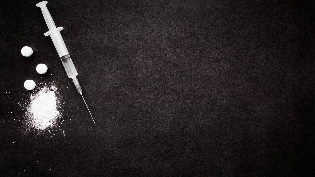Powder, tablets and syringe on dark black table.