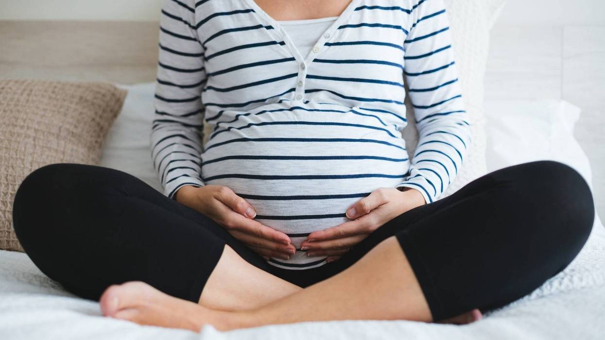 Pregnant woman in striped t-shirt sitting on the bed touching her belly