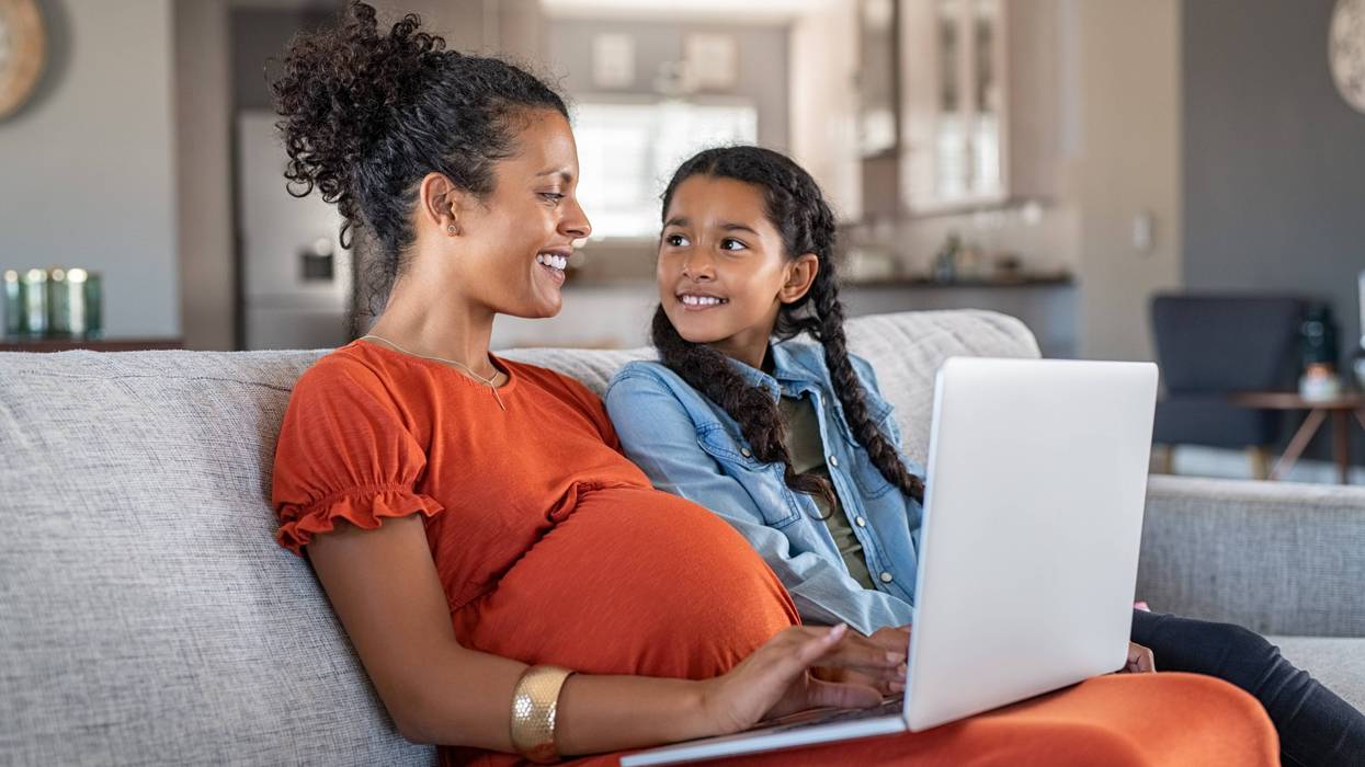Pregnant woman working from home in maternity leave as daughter looks on