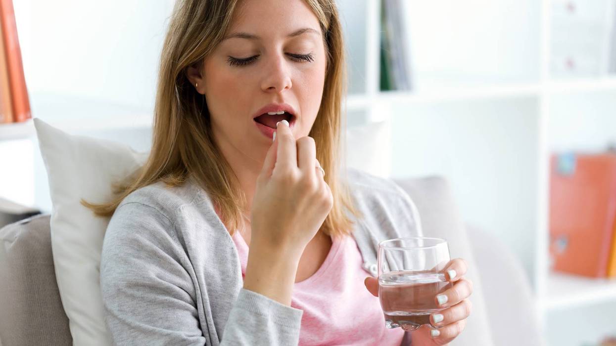 Pregnant young woman holding pill and glass of water at home