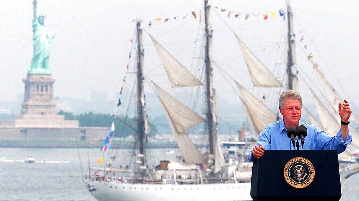 President Clinton speaks on the USS John F. Kennedy as a tall ship passes between him and the Statue of Liberty in New York Harbor during Independence Day celebrations in New York.