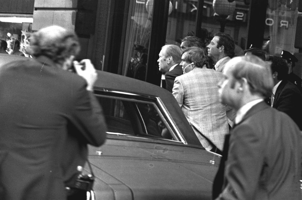 President Ford ducks behind his limousine and is hustled into the vehicle after a shot was fired as he left the St. Francis Hotel in San Francisco, Sept. 22, 1975. The president was rushed to the airport to return to Washington.