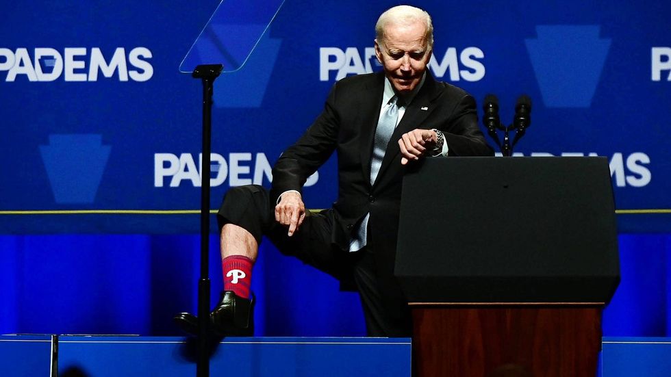President Joe Biden reveals a sock with the Philadelphia Phillies logo and checks his watch to see the time before the first game of the World Series as he addresses supporters during the Democratic Party