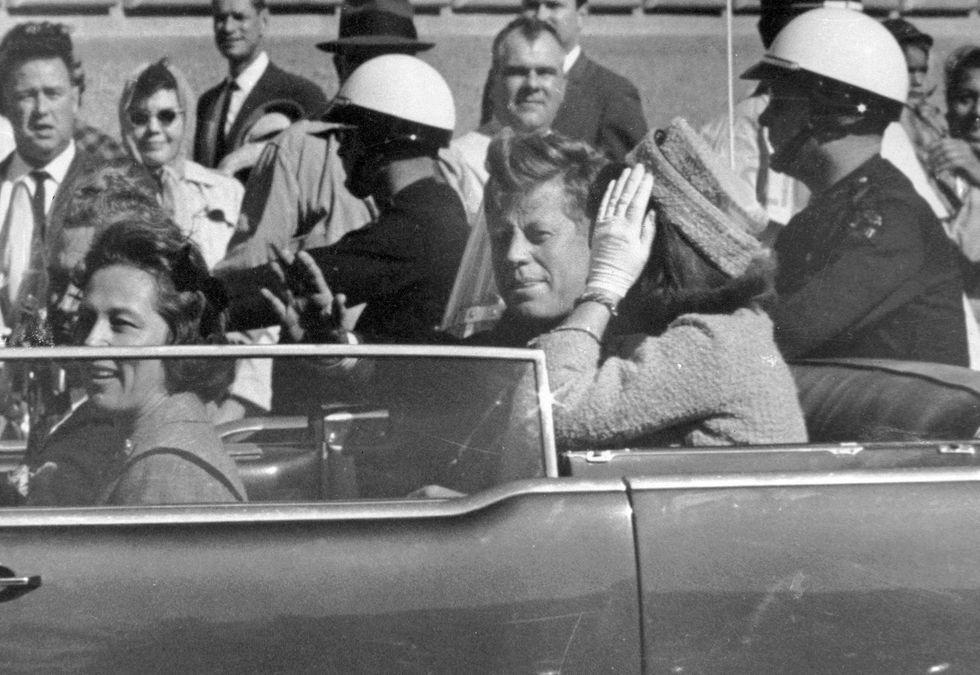 President John F. Kennedy waves from his car in a motorcade approximately one minute before he was shot on Nov. 22, 1963, in Dallas. Riding with President Kennedy are first lady Jacqueline Kennedy (right), Nellie Connally (second from left), and her husband, Texas Gov. John Connally (far left).