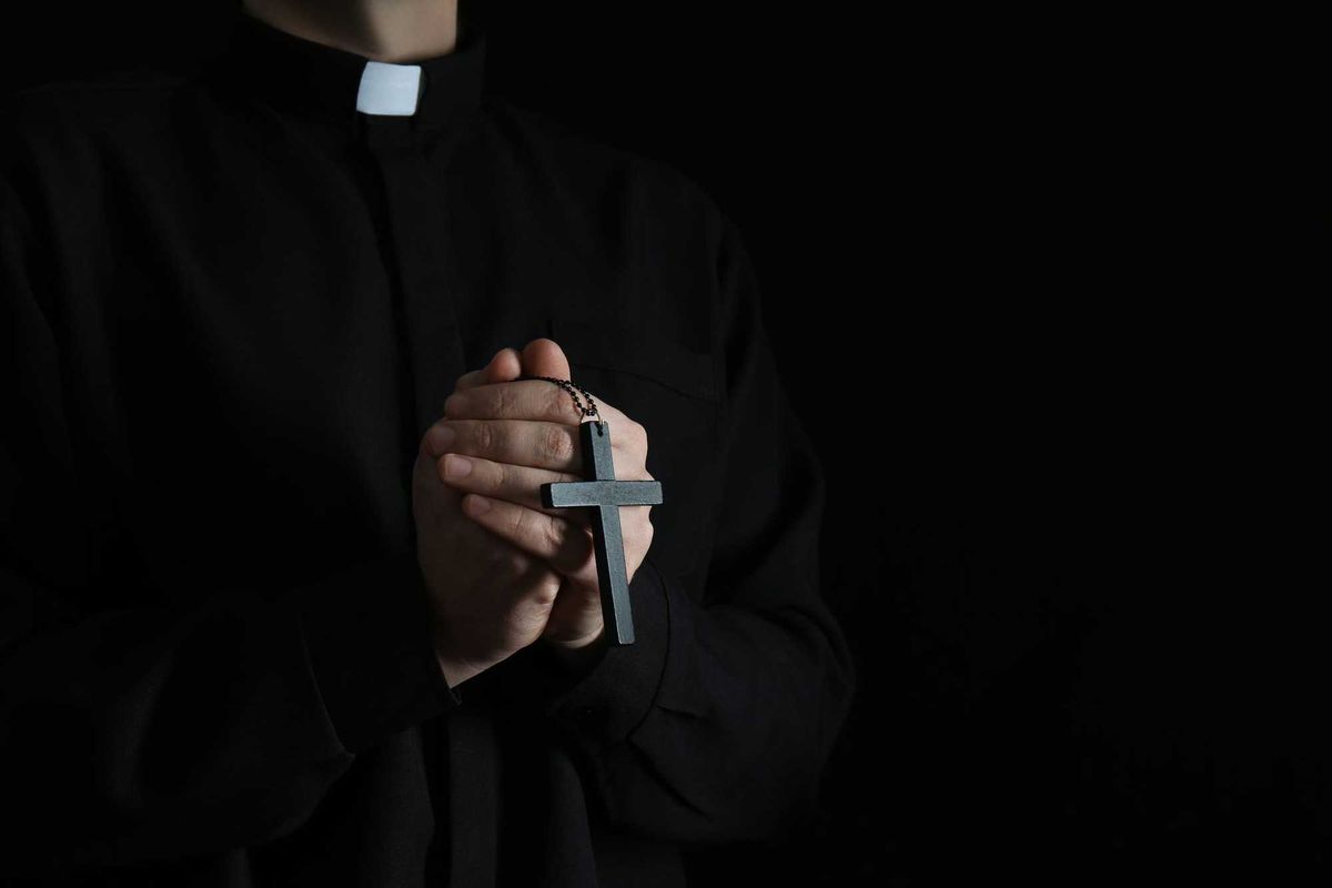 Priest with cross on dark background, closeup. Stock image.