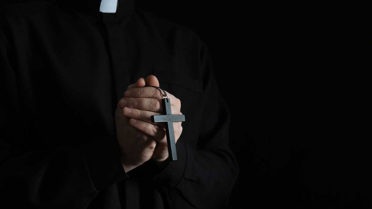 Priest with cross on dark background, closeup. Stock image.
