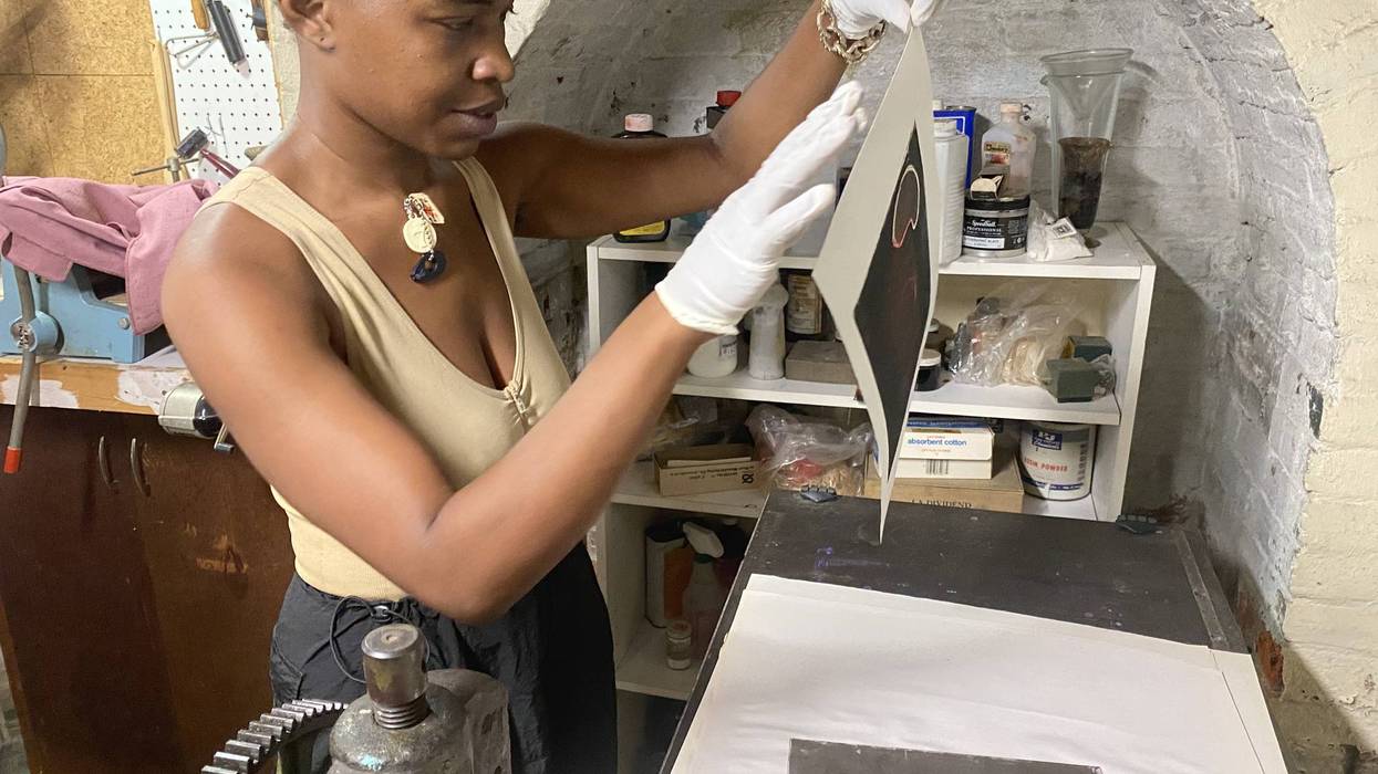 Printmaker in gloves carefully lifts a new print from a press
