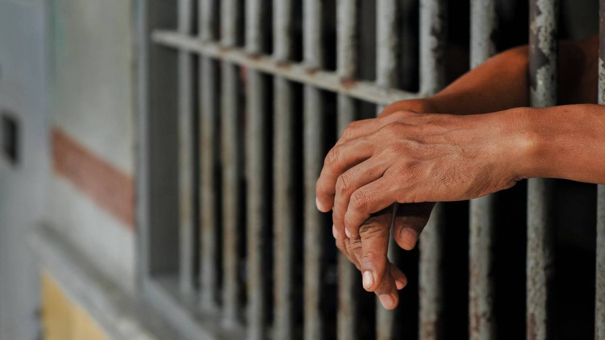 prisoner's hands behind bars with black background
