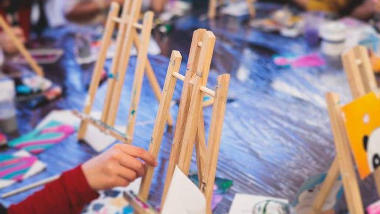 Process of painting, group class of young talented kids students with painting easels, and canvases during lesson of watercolour painting outdoors, drawing class for children in art school