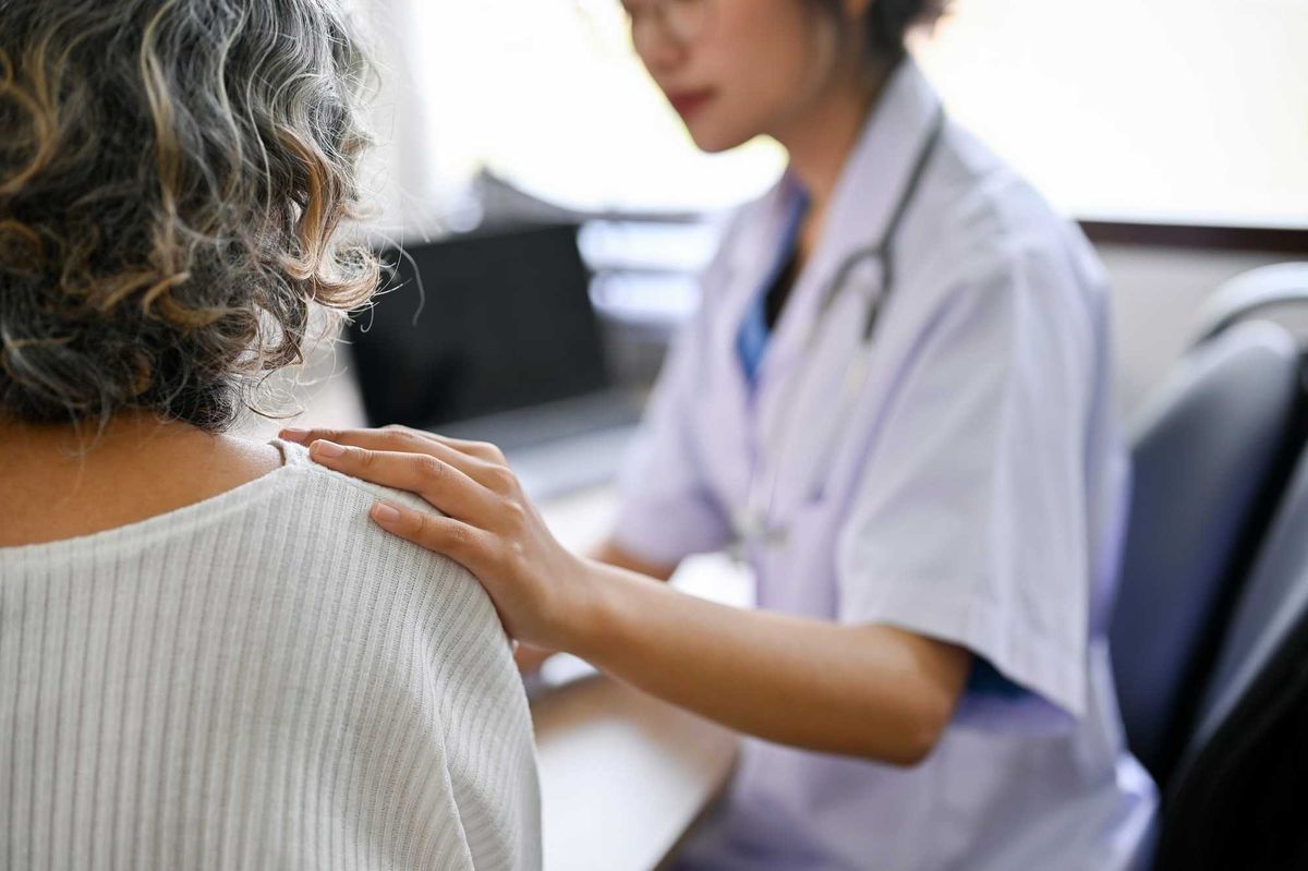 Professional Asian female doctor touching shoulder to comfort and support her patient. close-up image