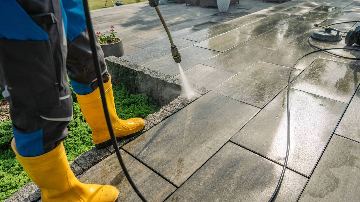 Professional Cleaning of Outdoor Stone Patio Using Pressure Washer and Protective Gear