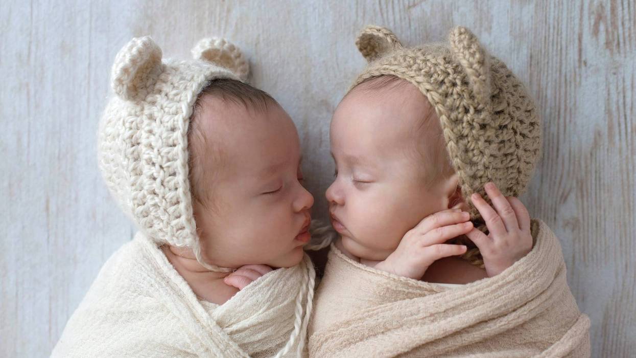 Profile headshot of two, fraternal, twin, baby girls sleeping. They are wearing crocheted bear hats and are swaddled in cream and tan wraps.