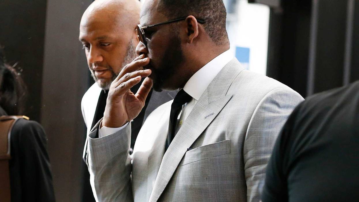 R. Kelly in a gray suit talks to a man next to him