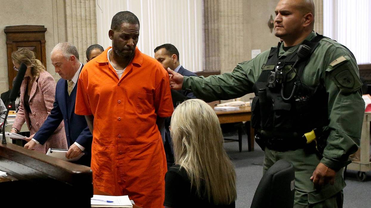 R. Kelly stands in a courtroom in a orange jumpsuit, while a guard escorts him out
