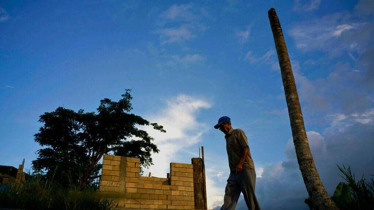 Ramon Alicea Burgos walks past his palm tree, with its top broken off one year ago by Hurricane Maria one outside his partially rebuilt home in the mountain town of Barranquitas, Puerto Rico.