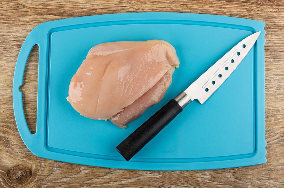 Raw chicken on a cutting board with a knife.