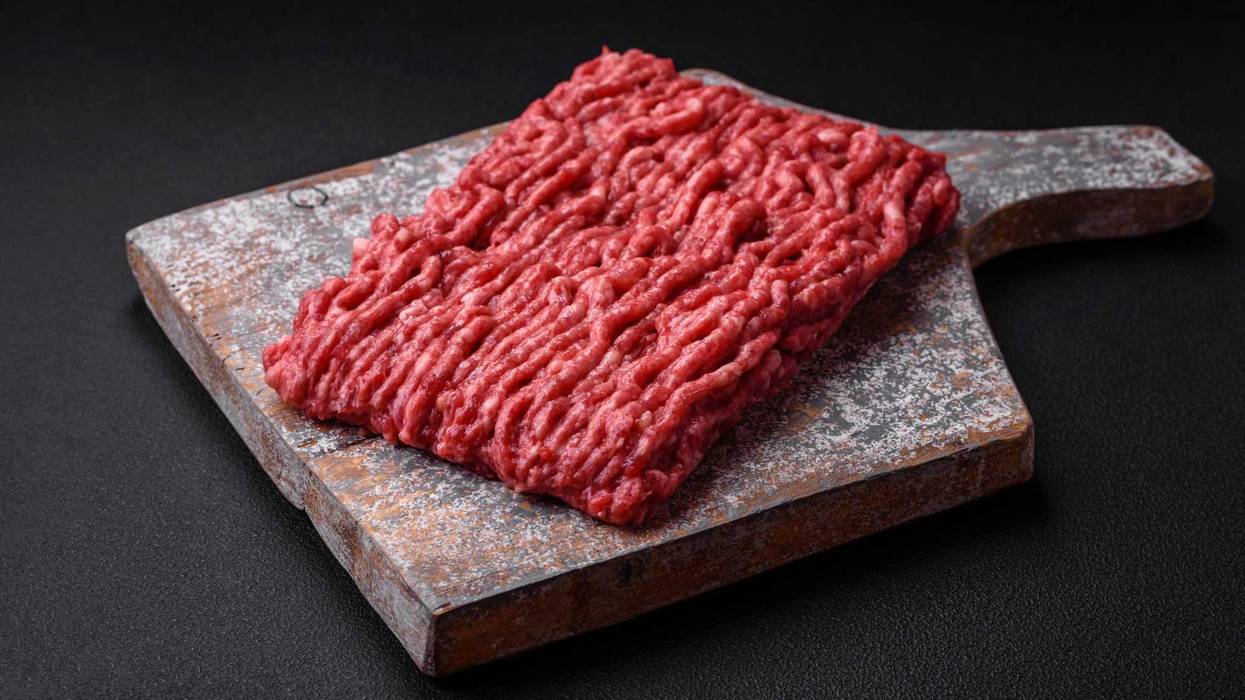 Raw ground beef or pork on a wooden cutting board with spices and salt on a dark concrete background