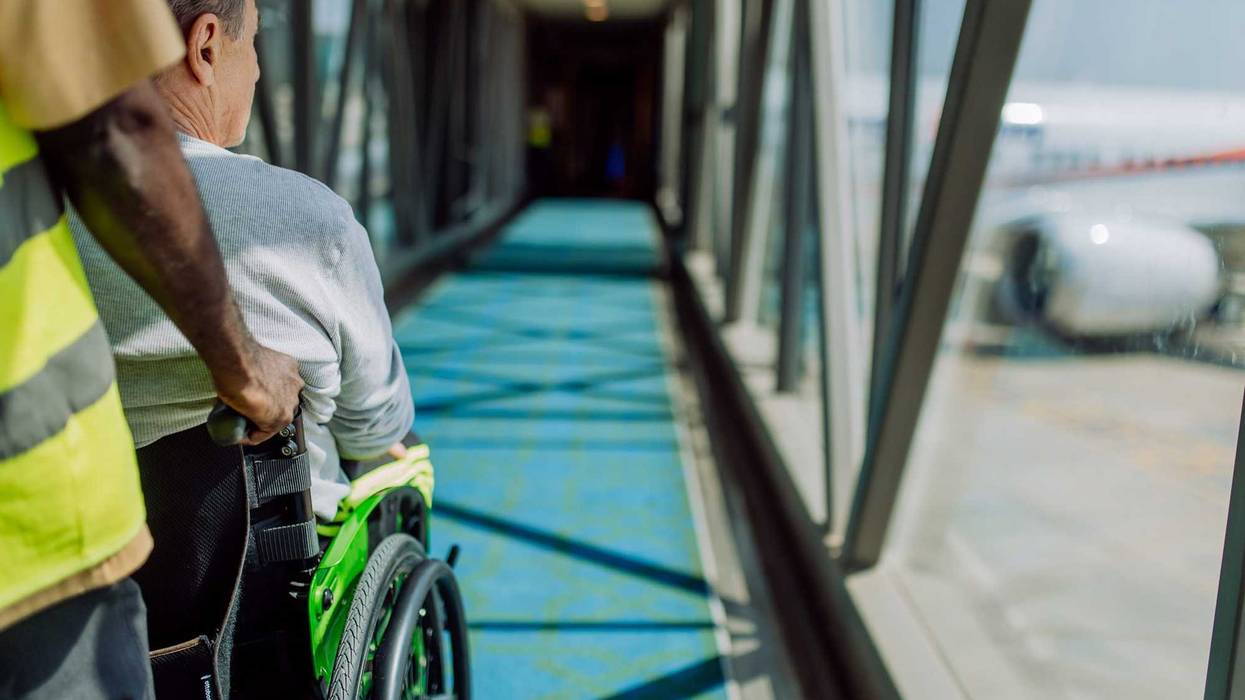 Rear view of an airport worker pushing man on wheelchair in the airplane. Concept of barrier-free travelling.