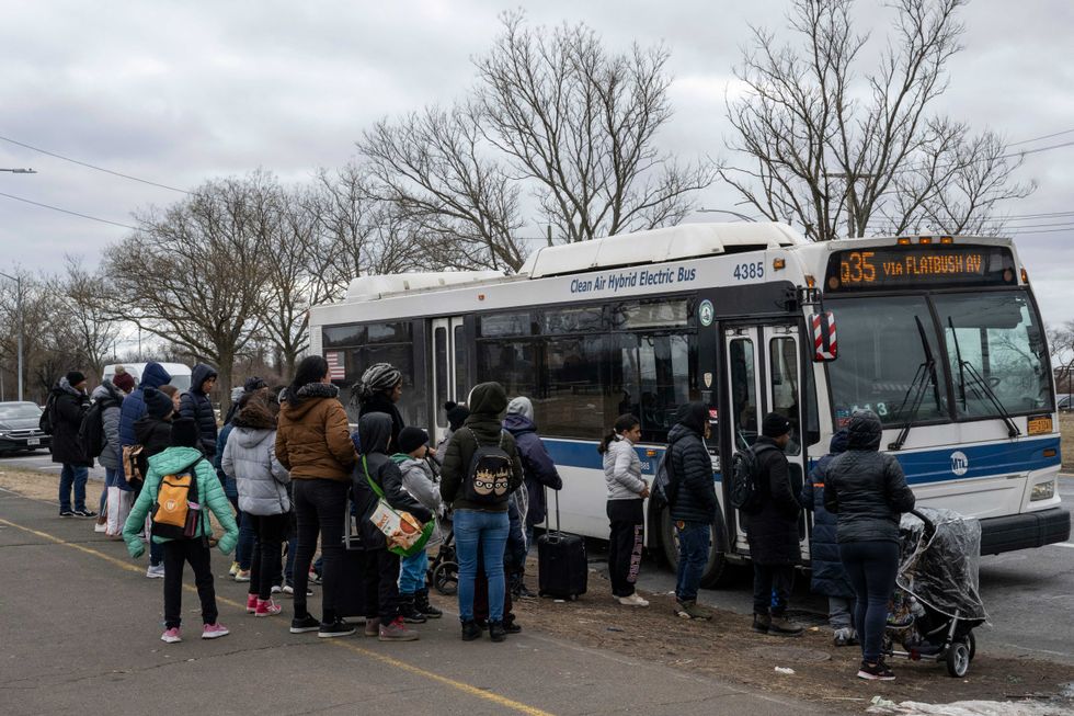 Recently arrived migrants wait at a bus stop outside Floyd Bennet Field shelter on February 21, 2024 in Brooklyn