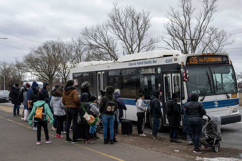 Recently arrived migrants wait at a bus stop outside Floyd Bennet Field shelter on February 21, 2024 in the Brooklyn borough of New York.