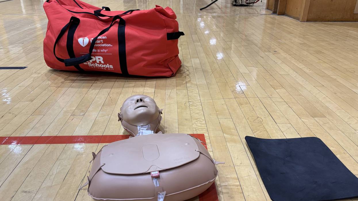 Red AHA CPR in Schools training bag and manikin on gym floor.