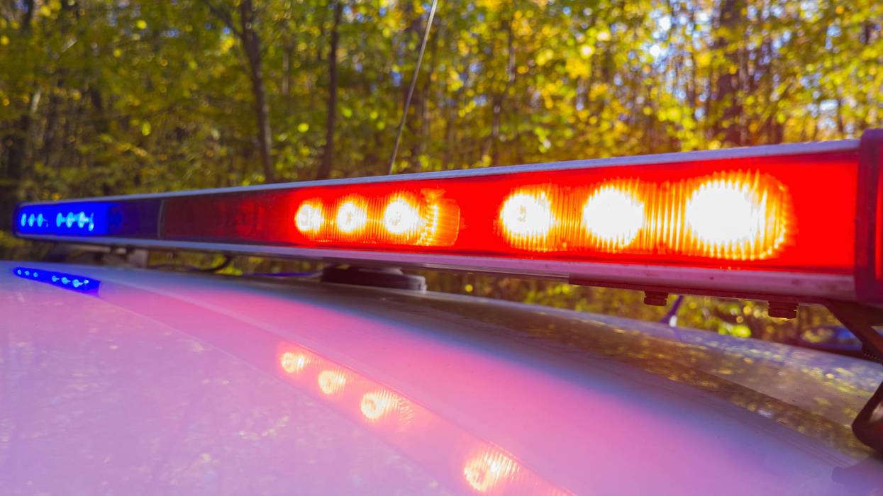 Red and blue flashing emergency lights on a vehicle roof, reflected, against autumn trees.