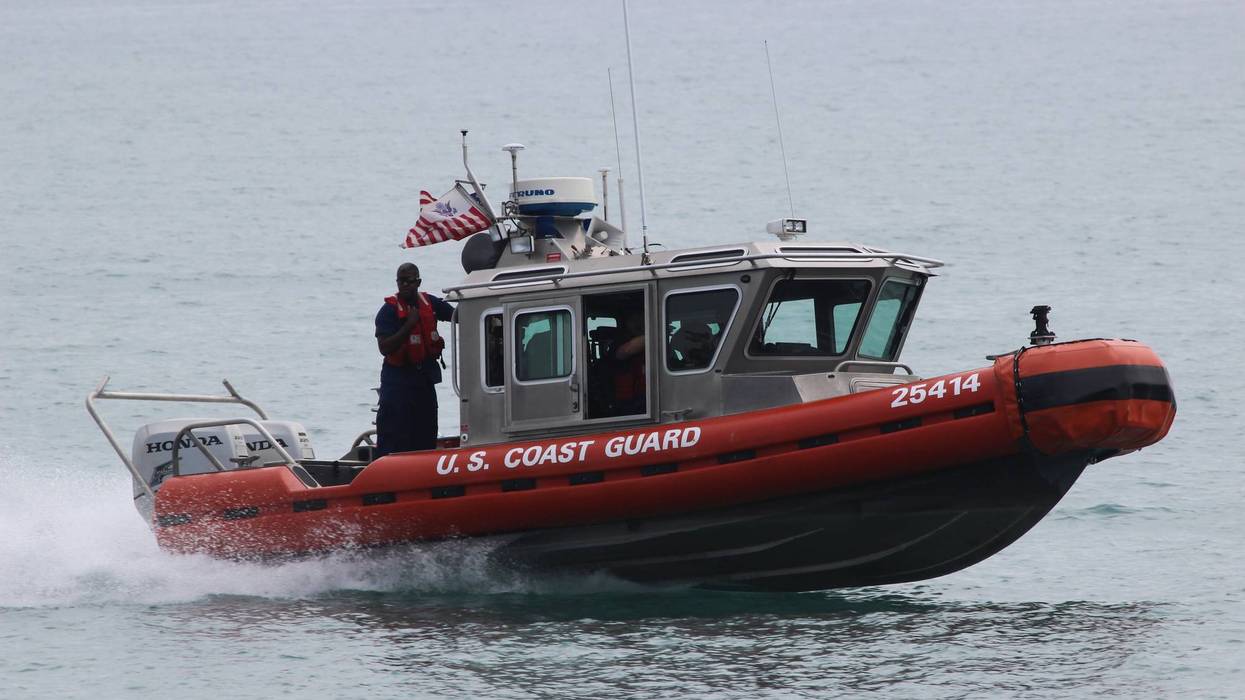 Red and gray U.S. Coast Guard boat 25414 with crew speeding on water.