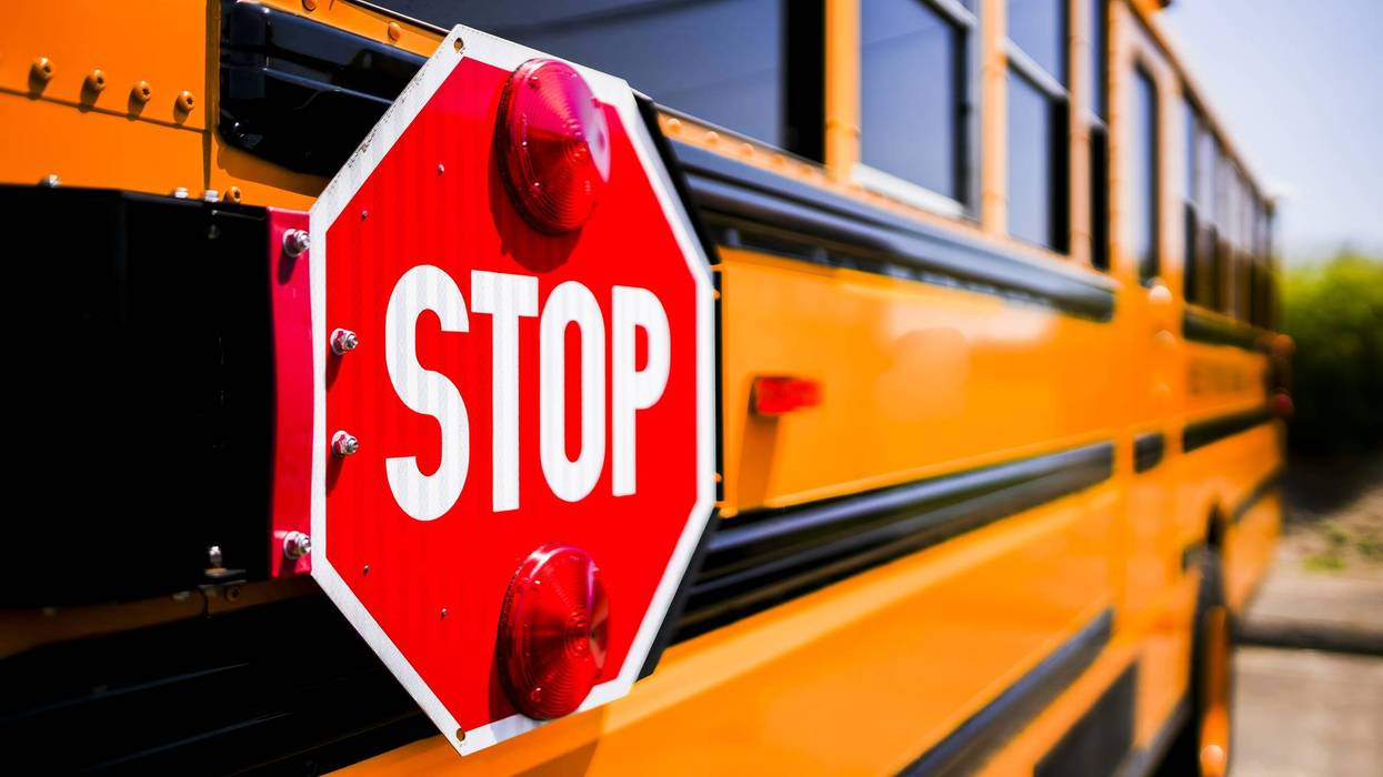 Red STOP sign with lights extended from the side of a yellow school bus.