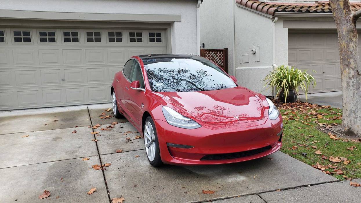 Red Tesla Model 3 automobile parked in the driveway of a suburban home.