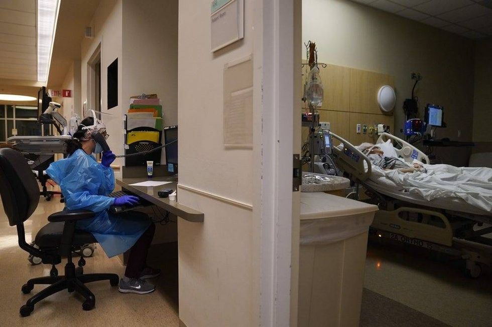 Registered nurse Melanie LaMadrid, left, talks on the phone as one of her patients lies in a bed in a COVID-19 unit.
