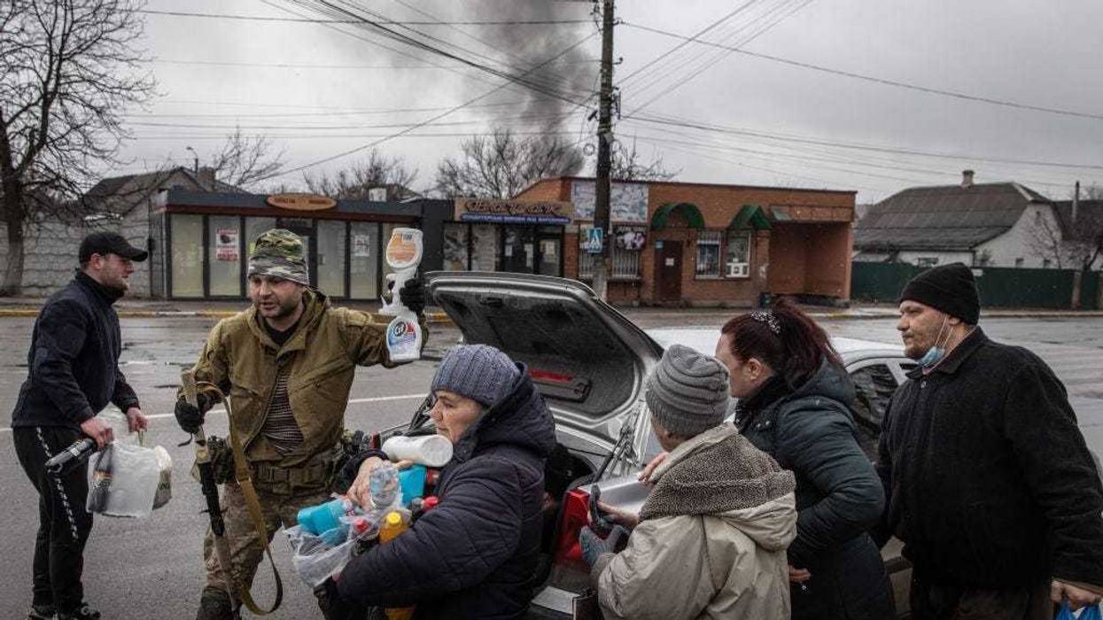 Residents crowd around to get food and other items handed out by members of the Ukrainian military as smoke rises from shelling on March 03, 2022 in Irpin, Ukraine.