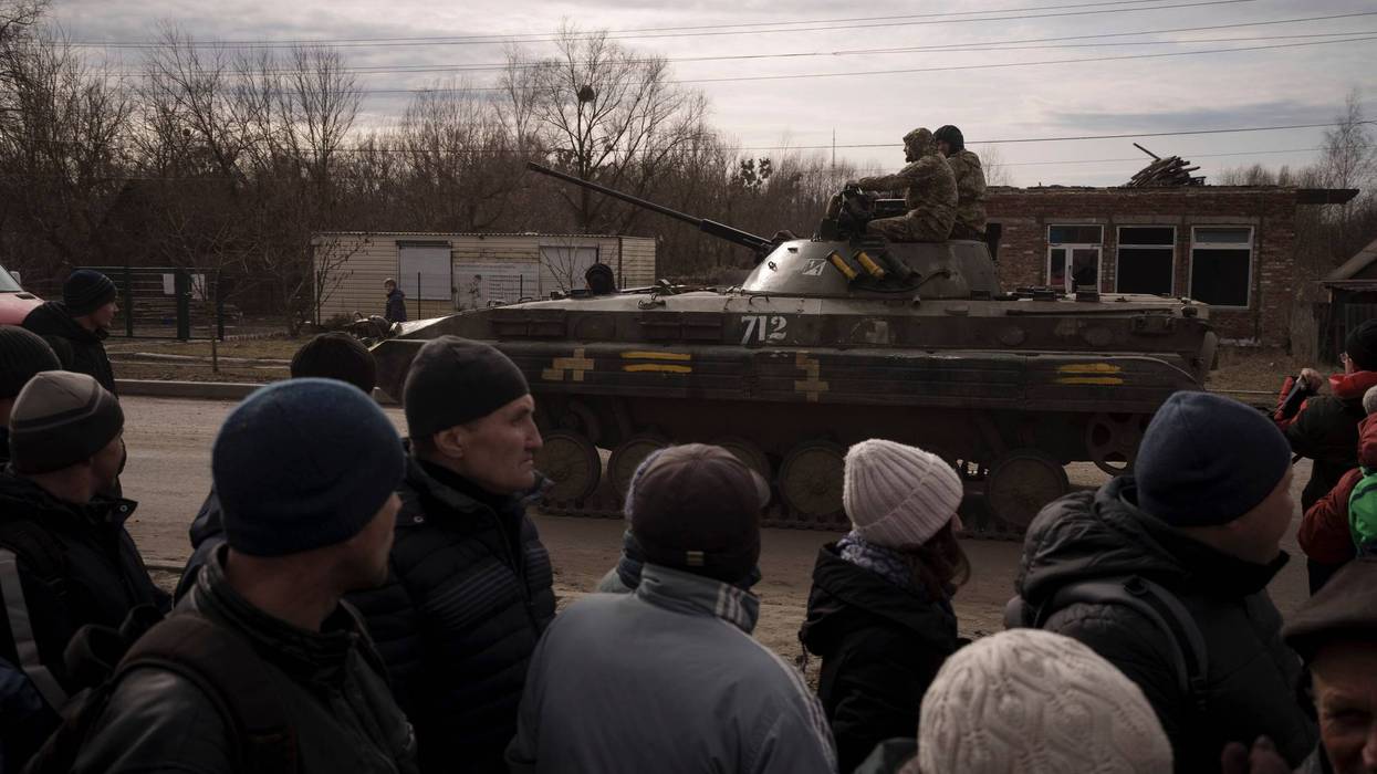 Residents lining up for aid watch as Ukrainian soldiers ride atop a tank in the town of Trostsyanets, Ukraine, Monday, March 28, 2022. Trostsyanets was recently retaken by Ukrainian forces after being held by Russians since the early days of the war.