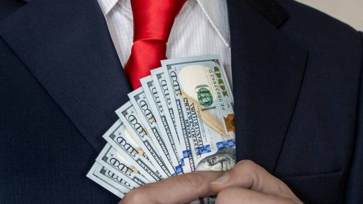 Rich man putting $100 bills into his suit pocket