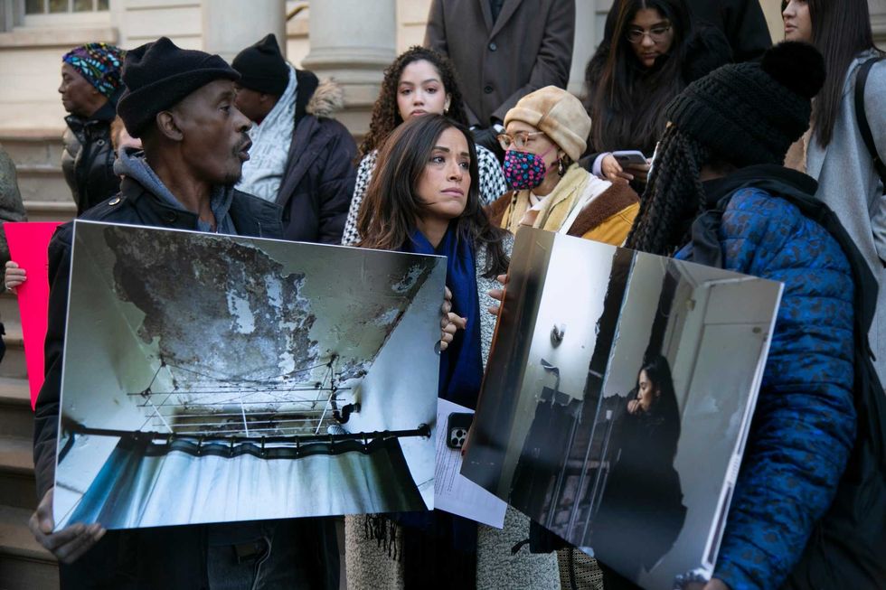 Rivera stands with NYCHA residents holding printed photographs of dilapidated apartments.