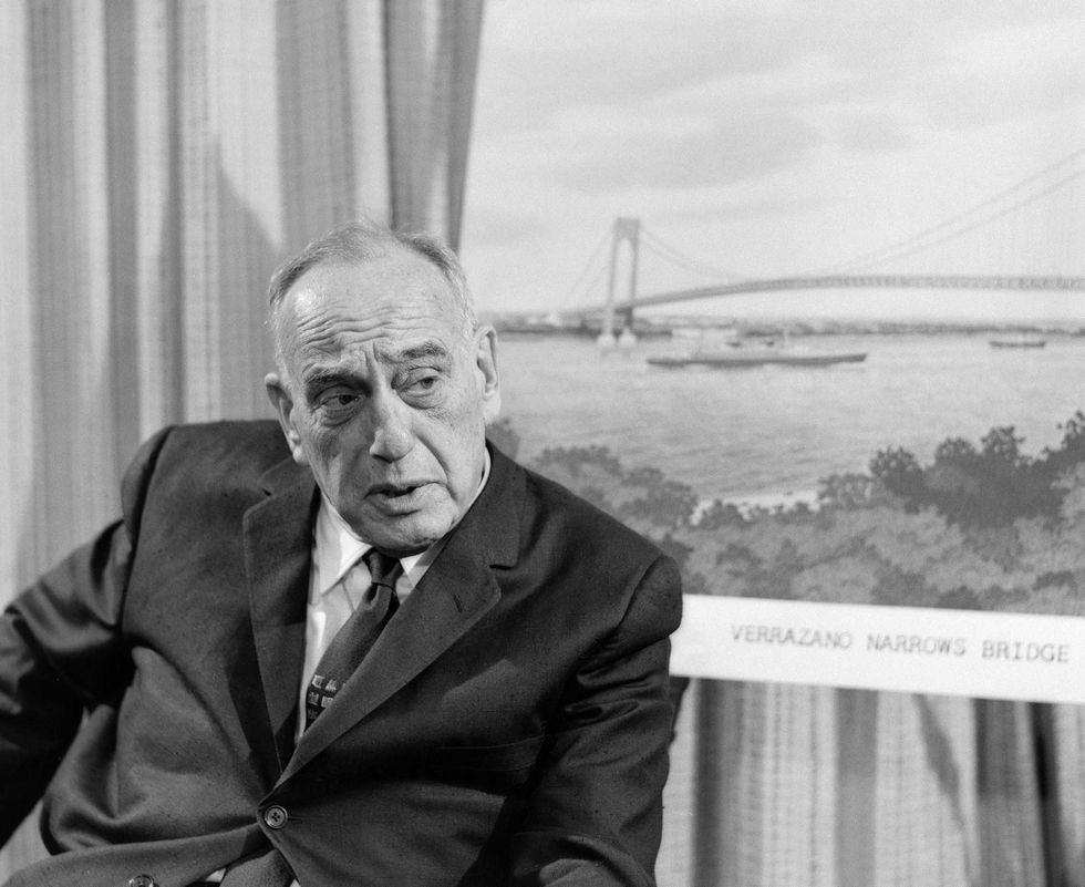 Robert Moses sits next to an illustration of the Verrazano Narrows Bridge (then nearly completed) during an interview for the
