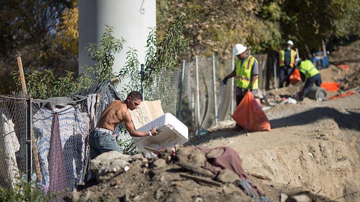 Rocky (L) cleans up the encampment of homeless friends who are faced with imminent eviction while they are away, as Cal Trans workers clean trash at a bridge construction site near the concreted channel of the Arroyo Seco Creek on November 20, 2015 in Los Angeles, California.