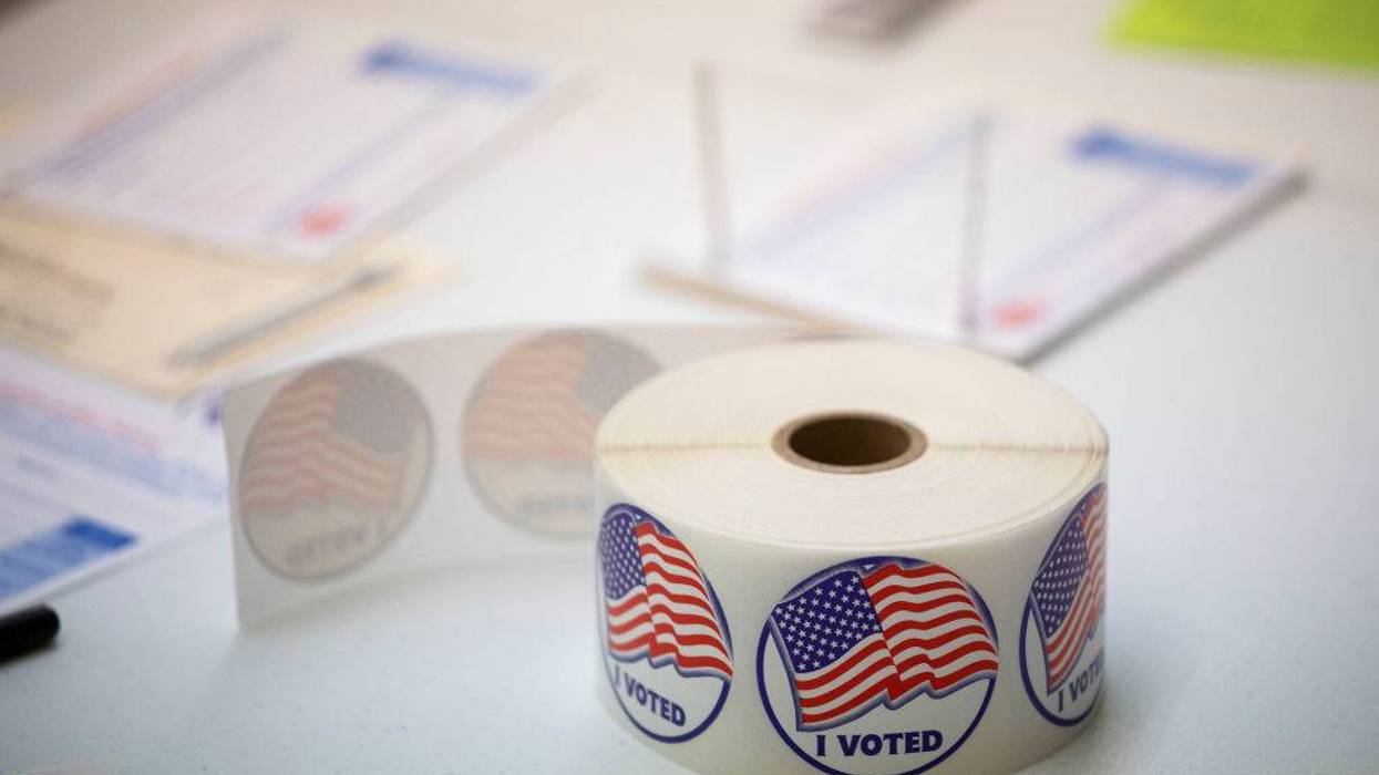 Roll of "I Voted" stickers with US flags on a table, blurred election forms in the background.