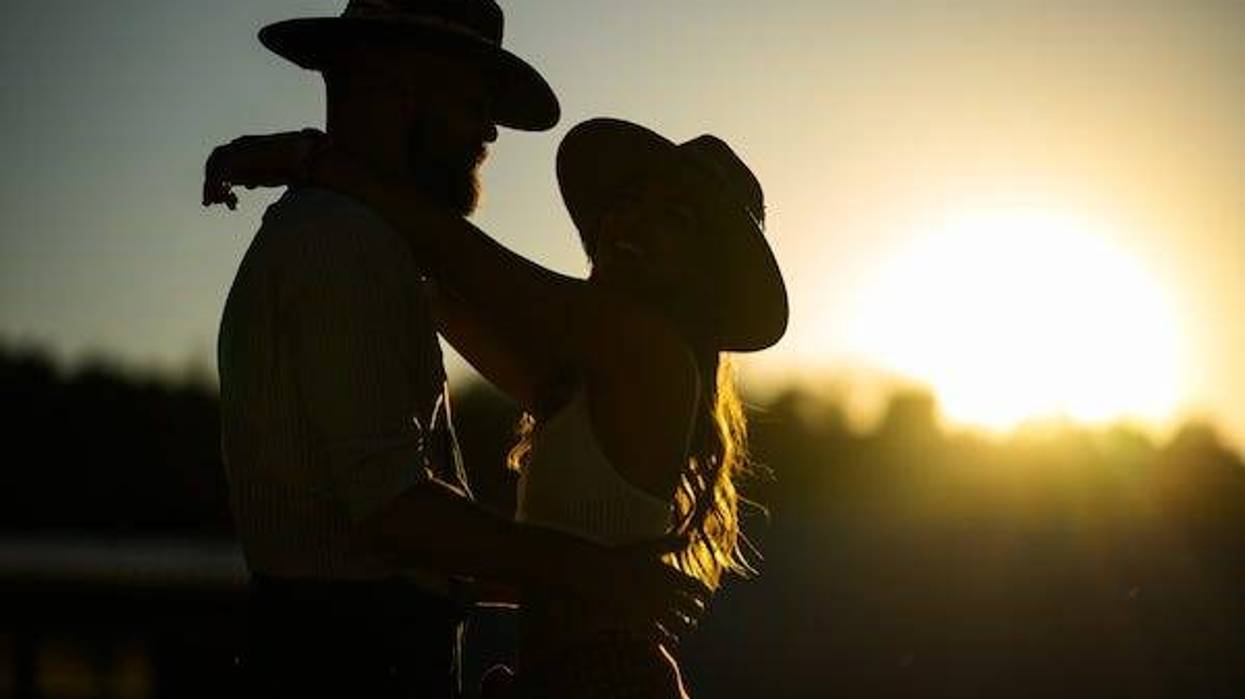 Romantic couple wearing cowboy hats posing in front of a sunset