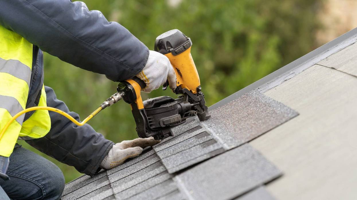 Roofer worker in uniform work wear using air or pneumatic nail gun