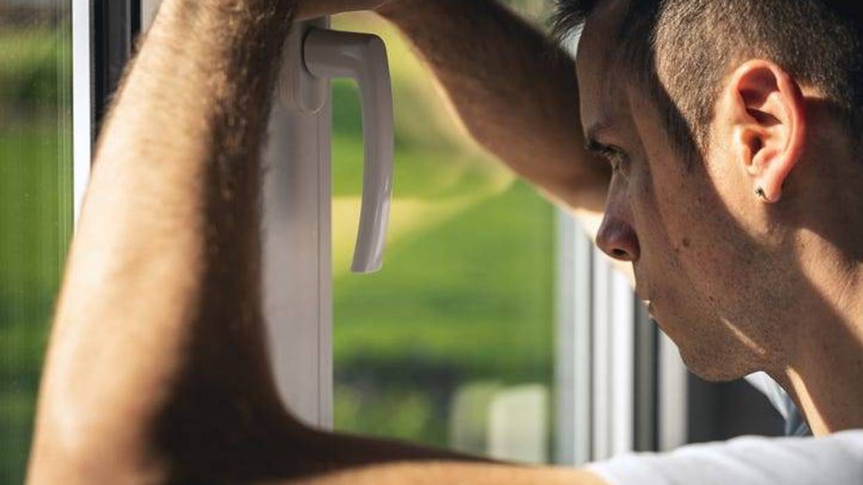 Sad, desperate young man looks out of window alone, symbol of hopelessness, fear, quarantine, sickness and mental health
